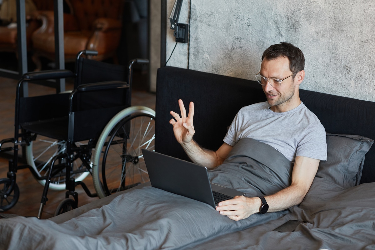 Disabled man having hypnotherapy online in bed Disabled man having hypnotherapy online on computer in bed