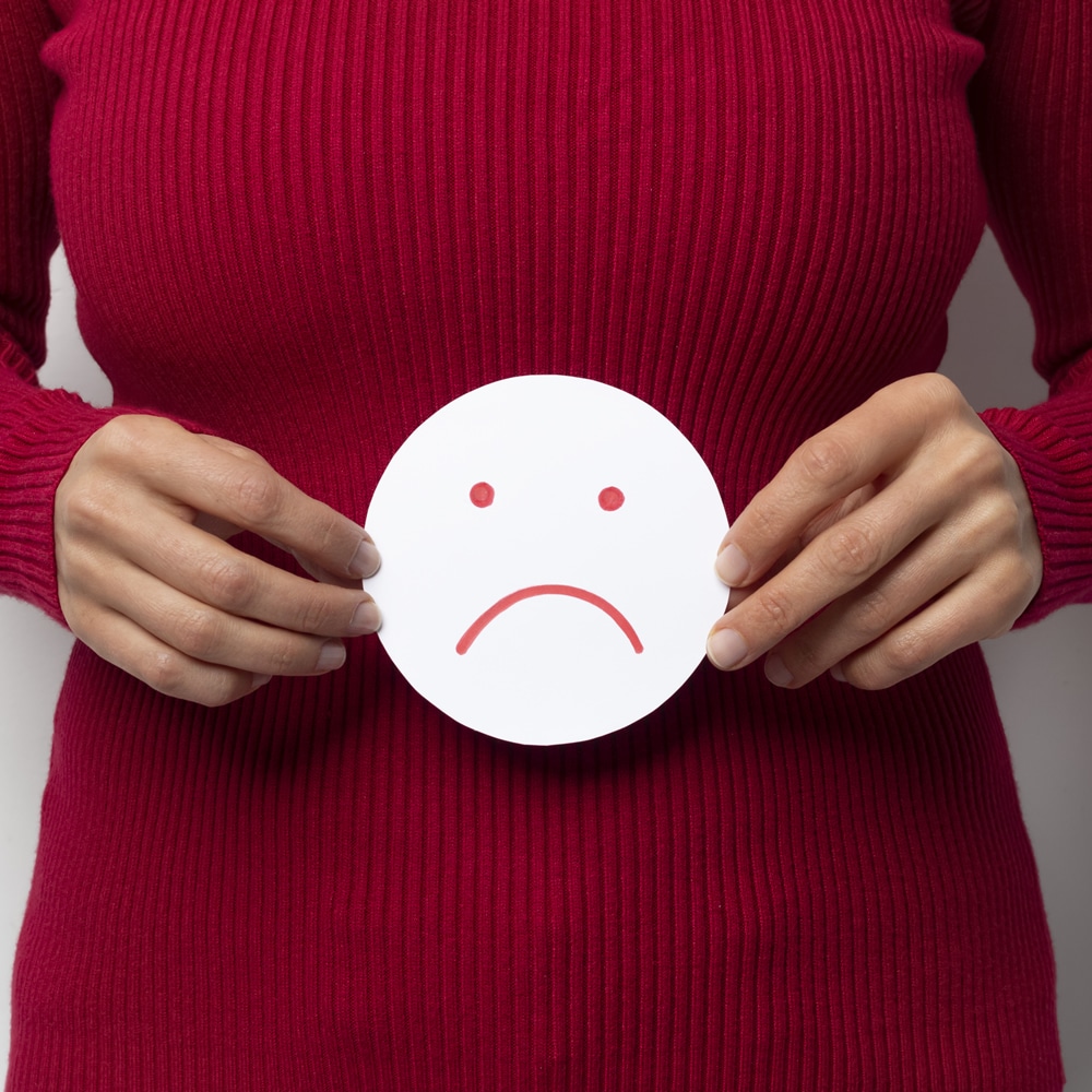 Woman with irritable bowel syndrome (IBS) Woman with irritable bowel syndrome (IBS), holding sad face sign